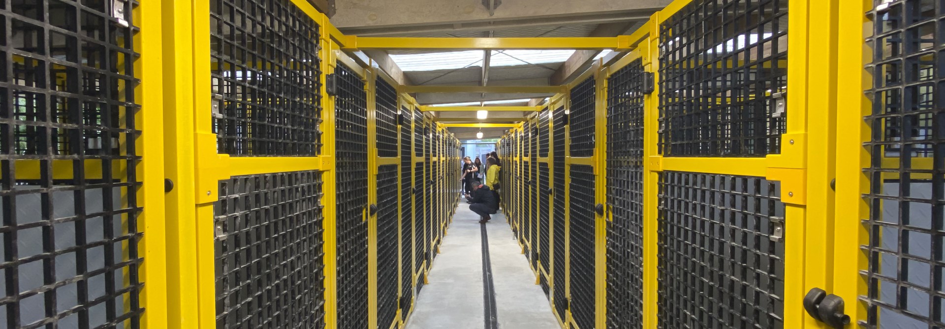 Inside the new Moa Point Animal Shelter, looking down a corridor, with concrete floor and black and yellow floor-to-ceiling caged rooms on either side.
