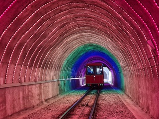 Photo from inside the Wellington Cable Car tunnel which is lit up bring pink with the cable car visible at the end of the tunnel. 