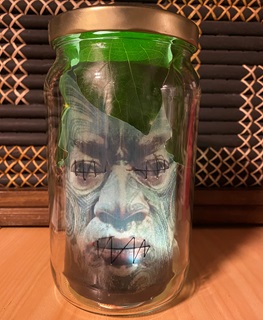 A jar with a photograph of a male face inside, with moko tattoos and leaves at the top near the lid.