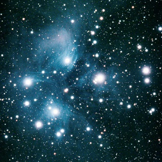 A photo of the Matariki star cluster, with its nine brightest stars clearly visible, along with hundreds of others that make up the cluster, on a bluey black sky.