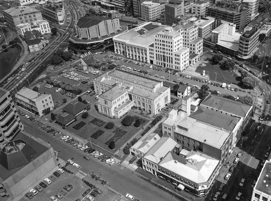 A black and white film photograph of a birds eye view of Wellington's Civic Square area in 1987, featuring the original city library, Town Hall, and lots of car parks.