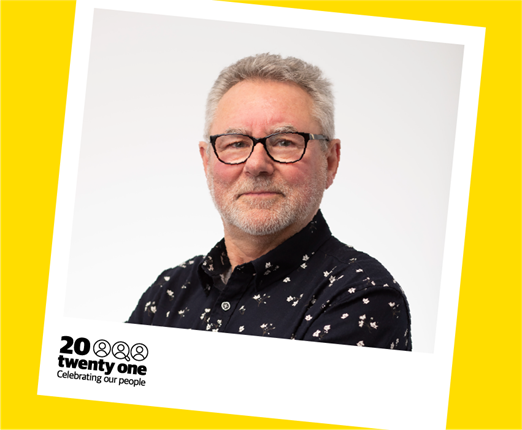 A portrait of Neil Price wearing black-framed glasses, and a dark shirt with small white flowers, in a polaroid frame that has the words 20 Twenty One, Celebrating Our People.