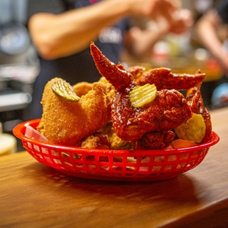 A red plastic basket full of spicy chicken wings and little slices of pickles.