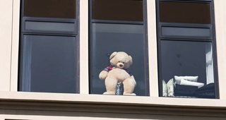 A large teddy bear in a window propped up on a vase.