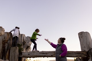 Two young girls and a woman climbing and balancing on a wooden play structure on Mount Victoria.