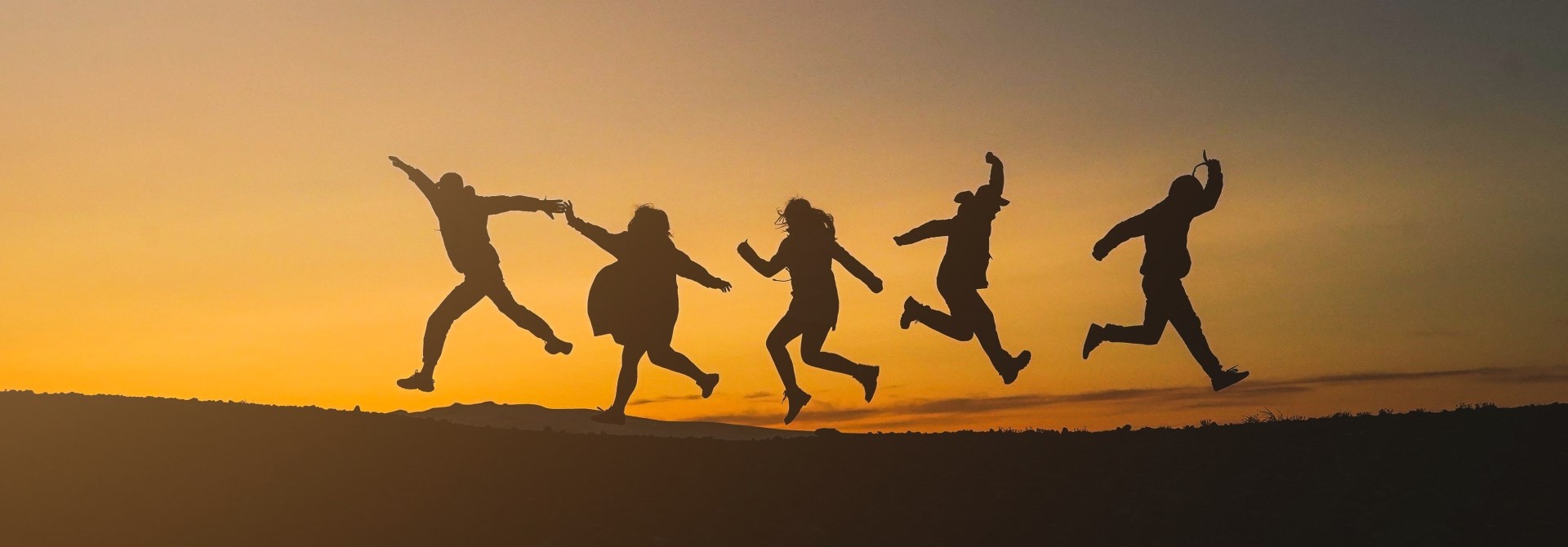 Silhouette of a group of people jumping for joy on a hill at dusk.
