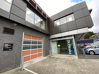 A flash new two-storey grey building, with a red panelled garage delivery door and the words Te Pātaka painted in white on the glass entry door, and cars parked outside.