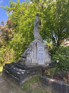 A gravestone on the back of a large sculpture of a man.