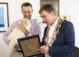 Mayor Andy Foster reading the Key to the City certificate to Mittens the cat who is being held up by his owner Silvio.