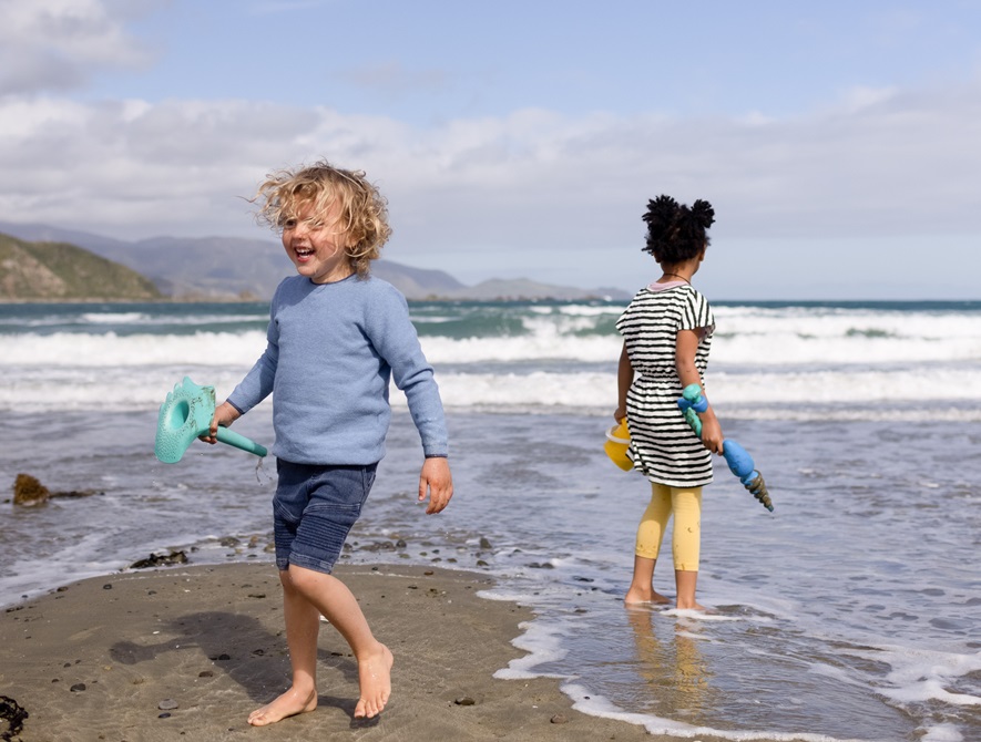 Two children holding buckets and spades, playing on the shore of Lyall Bay beach.