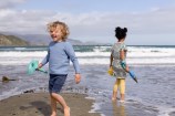 Two children holding buckets and spades, playing on the shore of Lyall Bay beach.