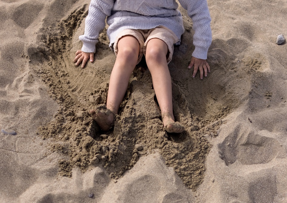 A child sitting in the sand, playing with their hands and feet.