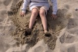 A child sitting in the sand, playing with their hands and feet.