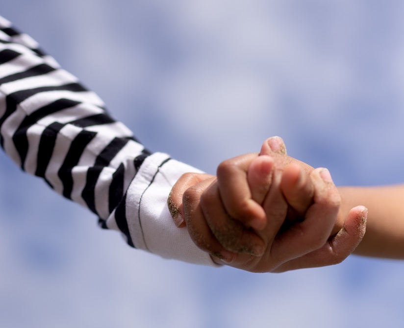 Two children's hands holding one another with a blue sky in the background.