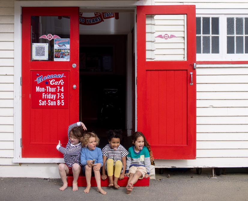 Four children sitting in the doorway of Maranui cafe in Lyall Bay.