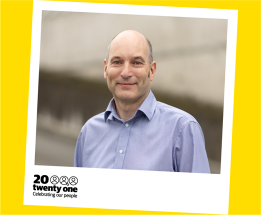 A smiling middle-aged pakeha man wearing a tidy blue shirt, pictured in a polaroid with the words '20 Twenty One: Celebrating our People' printed on the bottom left.