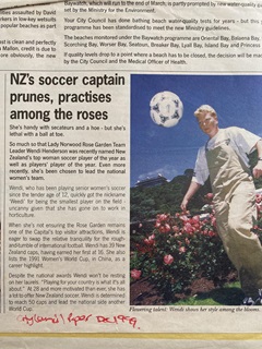 A newspaper clipping with a woman dressed in white kicking a football, with the headline reading 'NZ's soccer captain prunes, practises among the roses'.