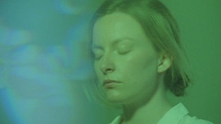 A still of a film showing a woman with her eyes clothes bathed in blue and green light.