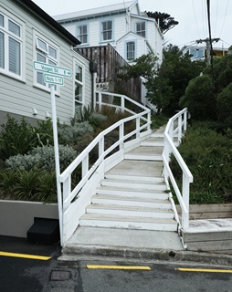 Concrete stairs and white handrails sit beside houses, with a sign that reads 