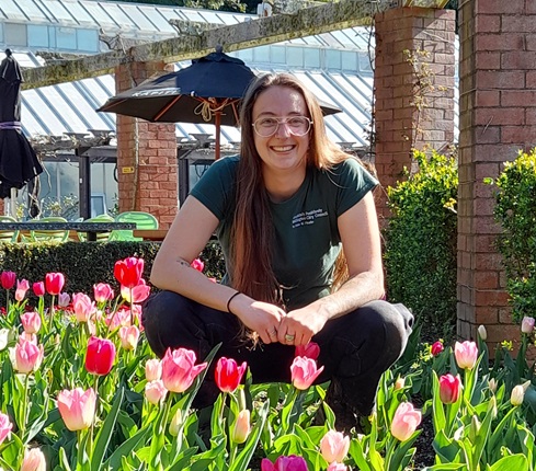 Cheyney smiling and crouching behind a bed of tulips at the Botanic Gardens.