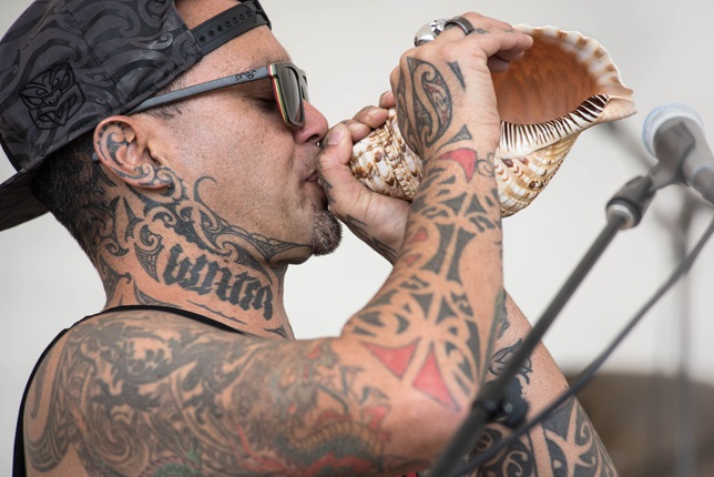 Tiki Taane using a conch shell at a music festival in Paihia