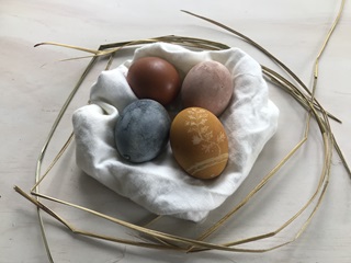 Eggs coloured in natural dye for Easter, laid out on a white clothe on a white marble bench.