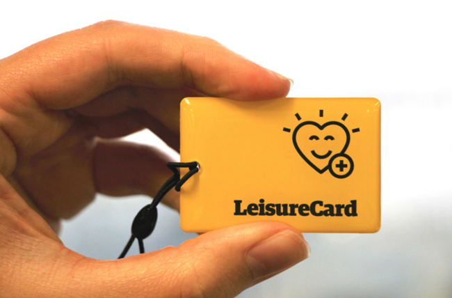 A hand holding a small shinny yellow card with the word 'LeisureCard' on it as well as simple smiley face heart illustration.