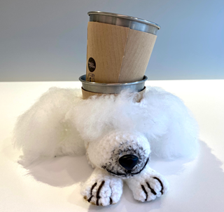 A silly white-knitted poodle cup holder, with two reusable takeaway cups stacked inside it.