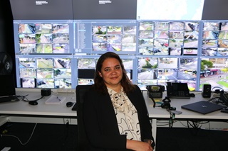 Woman sitting on a chair in front of a wall of screens showing CCTV footage.
