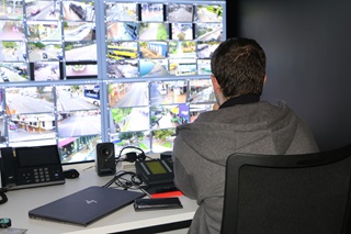 Man sitting at a desk looking at a wall of screens with CCTV footage.