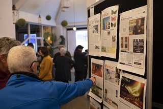 Two people point and read printed copies of City Voice paper on a presentation board.