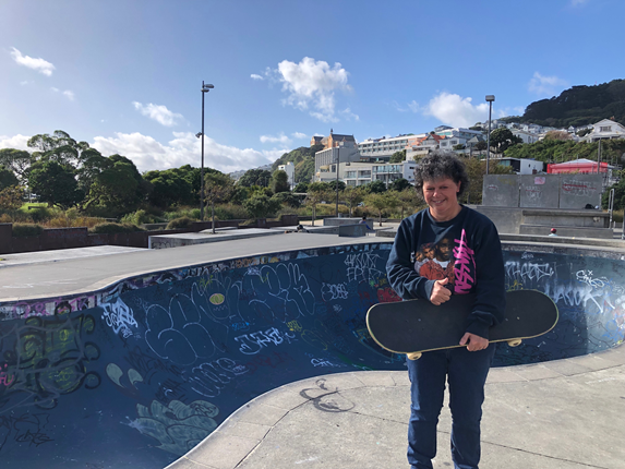 Woman standing in front of skating bowl whilst holding a skateboard.