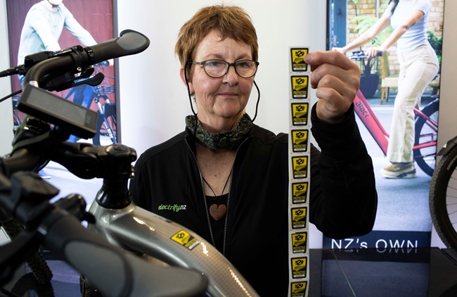 Owner of Wellington Electrify NZ shop holding 529 stickers next to bike