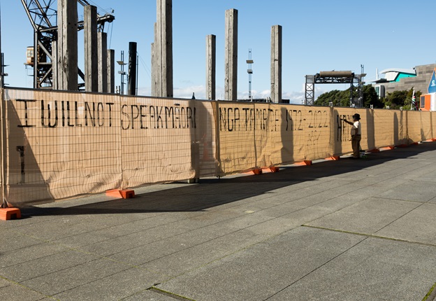 Tame Iti painting ‘I Will Not Speak Māori’ in big bold letters across Wellington’s waterfront.