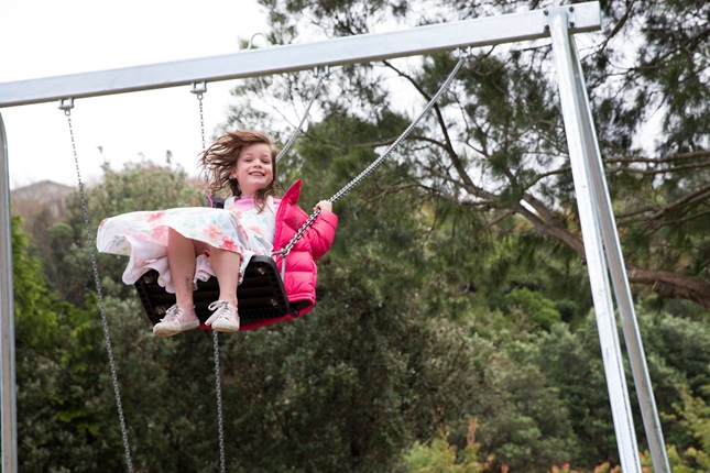Child on a swing wearing a pink jacket.