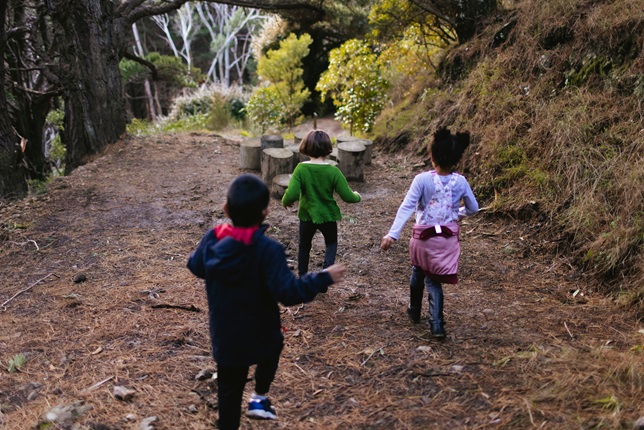 Three young children running down hill in park area