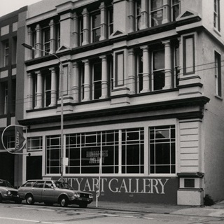 A black and white photo of the city gallery with a car parked outfront.