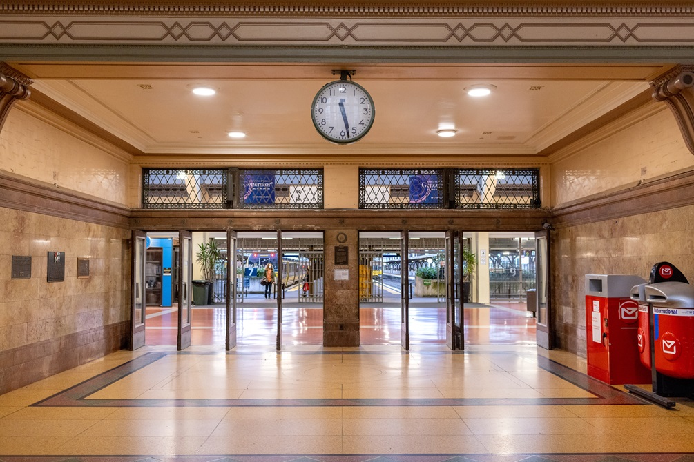 The eight doorways into the Wellington Railway Station, with the detailed ceiling and large black and white clock in the foreground. A red post box is to the right.