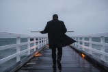 A man walking down a pier wearing a black coat.