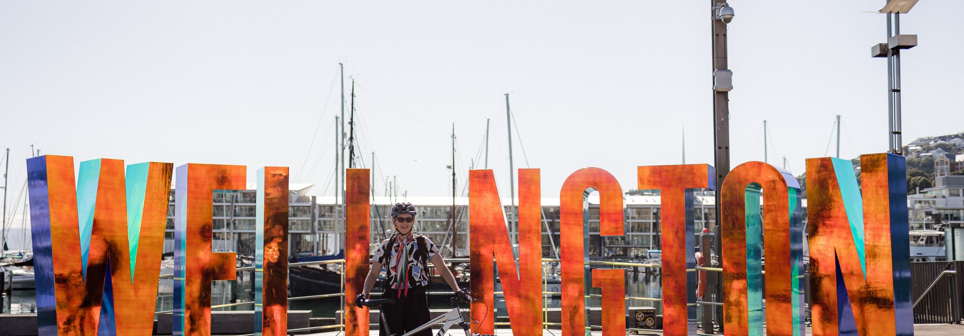 Woman standing behind her bike, infront of the 'Well_ngton' sign.