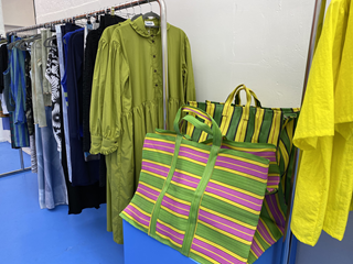 Items in a shop with a stripey pink and green bag with clothes hanging on a rack.