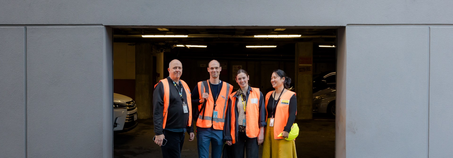 A group of four people standing in a row wearing orange high vis jackets.