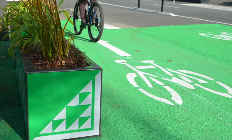 Cyclist on new Basin Reserve to Sea bike lane going past green and white planter boxes.