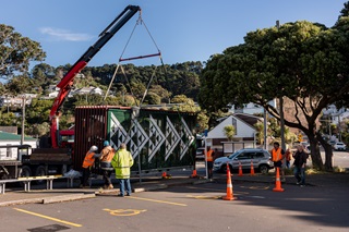Crane installing a bike shelter infront of a swimming pool with road cones on the ground.
