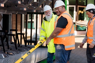 Three men in high vis with white hard hats on working to install a bike shelter.