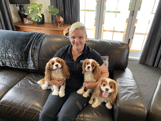 Woman sitting on the couch with three Cavalier King Charles Spaniels on her lap.