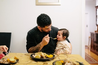 Man feeding his small child at the dinner table.