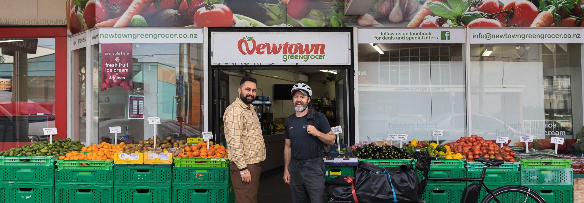 Two people standing outside of a Greengrocer in Newtown with an ebike and veges out front.
