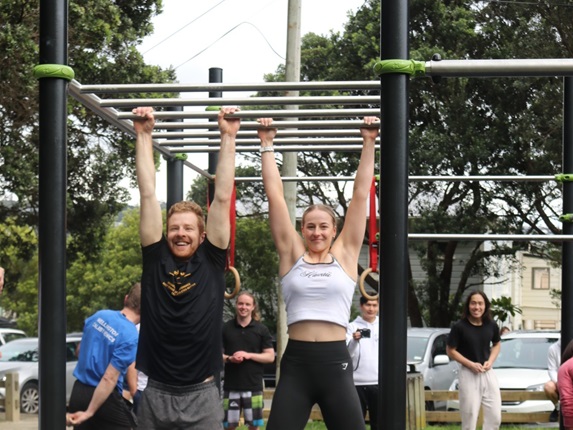 A man and a woman hanging down from monkey bars in a calisthenics park.