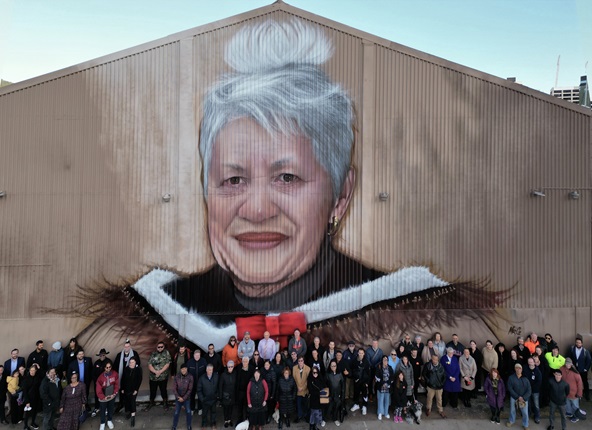 Drone shot of June Jackson mural by Mr G on side of Shed 1 on waterfront with attendees at blessing in foreground